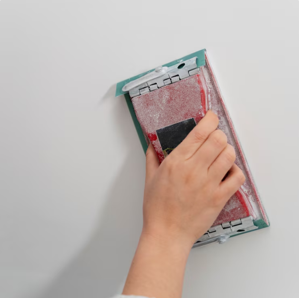 hand smoothing drywall surface with sanding tool