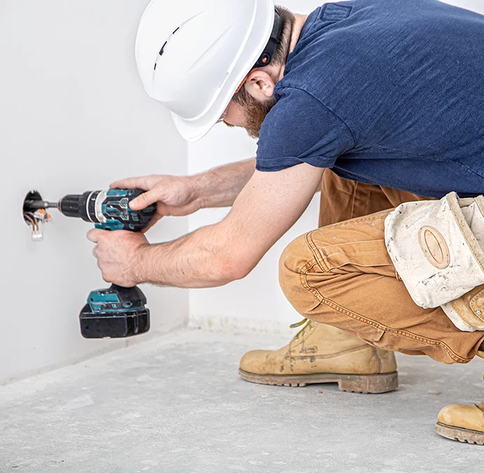 Drywall technician drilling near outlet - expert drywall services Burlington by Express Drywall Services.