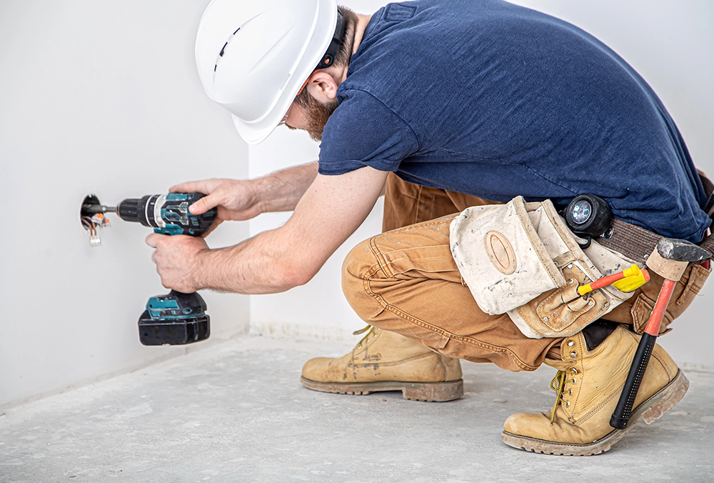 Drywall technician drilling near outlet - expert drywall services Burlington by Express Drywall Services.