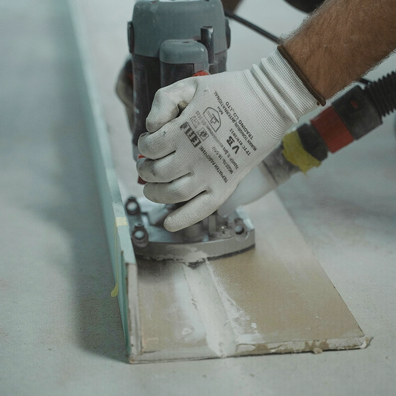 A Express Drywall Services worker preps a panel edge during commercial drywall installation using a precision router tool.