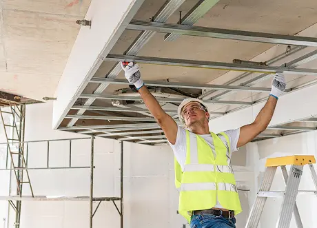 Worker installing suspended framing for a commercial T-Bar and drop ceiling system.