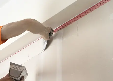 Worker applies fire caulking to drywall corner at a commercial site.