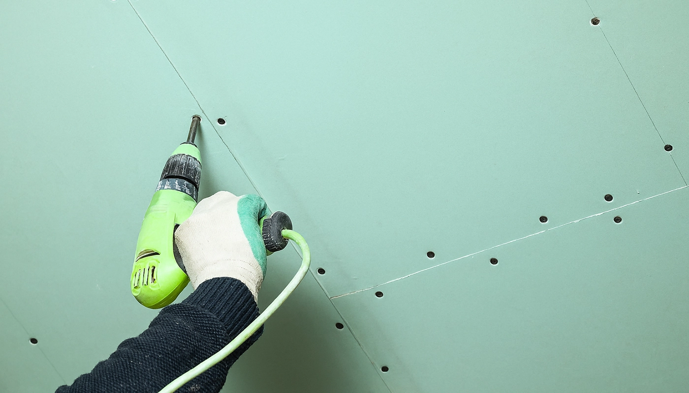 Worker securing green moisture-resistant drywall during ceiling installation – part of a moisture-resistant drywall installation and tile backer in Toronto by Drywall Express Services.