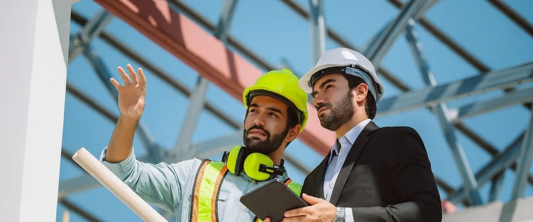 Construction manager and contractor discussing project plans on-site, wearing lime green safety gear, representing the importance of choosing the right framing and drywall partner with Express Drywall Services.