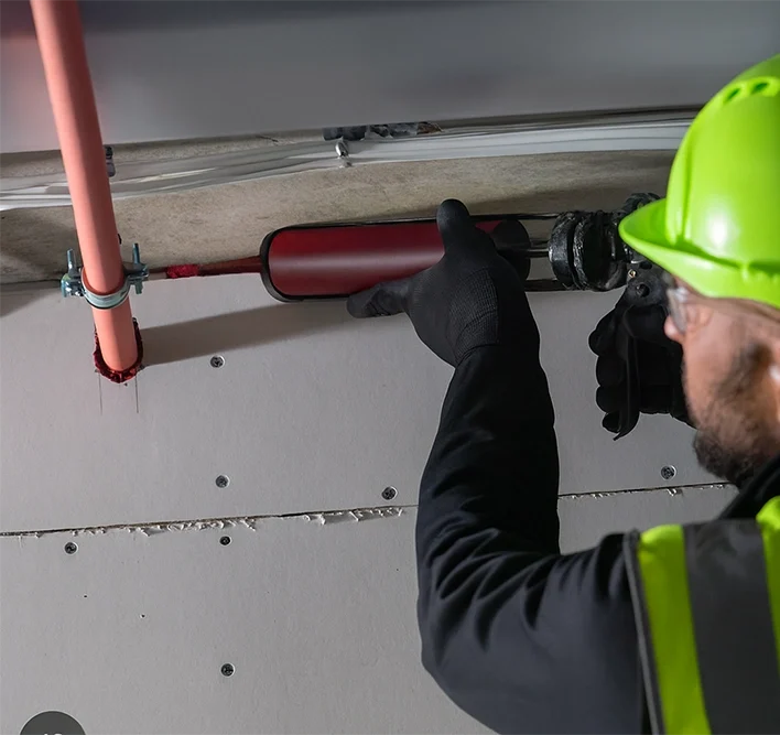 Technician applying commercial fire caulking around pipe penetration — Commercial Fire Caulking in Toronto by Express Drywall Services