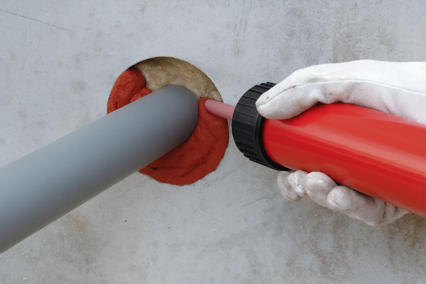 Technician applying red fire caulk around plastic pipe penetration during fire caulking in Richmond Hill.