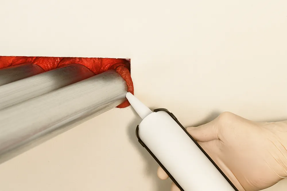 Applying red fire caulk around grouped metal pipes during fire caulking in Richmond Hill.