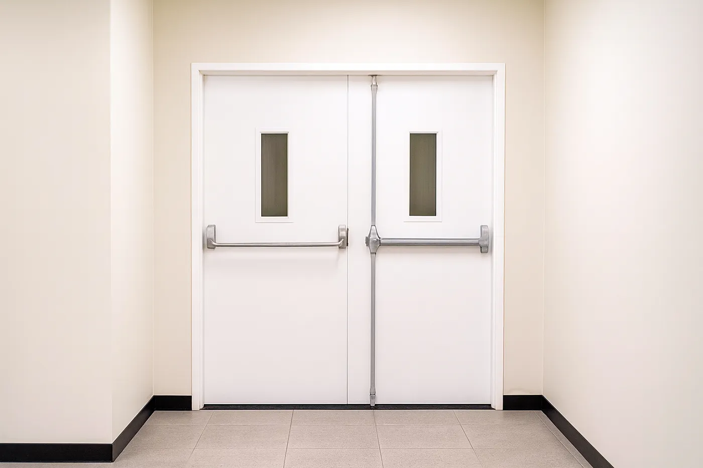Commercial metal door installation in Richmond Hill – double white steel doors with panic bars in a commercial hallway.
